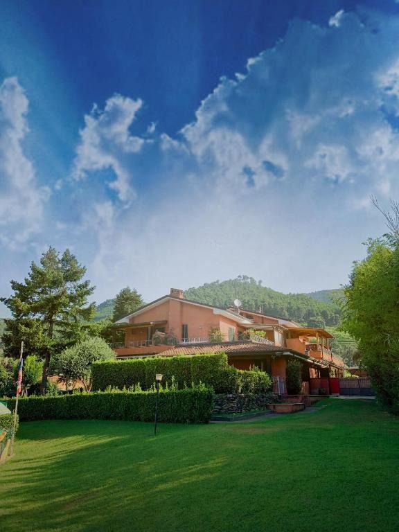 Casa con tetto di tegole rosse, prato verde e siepi sotto un cielo azzurro con nuvole bianche.