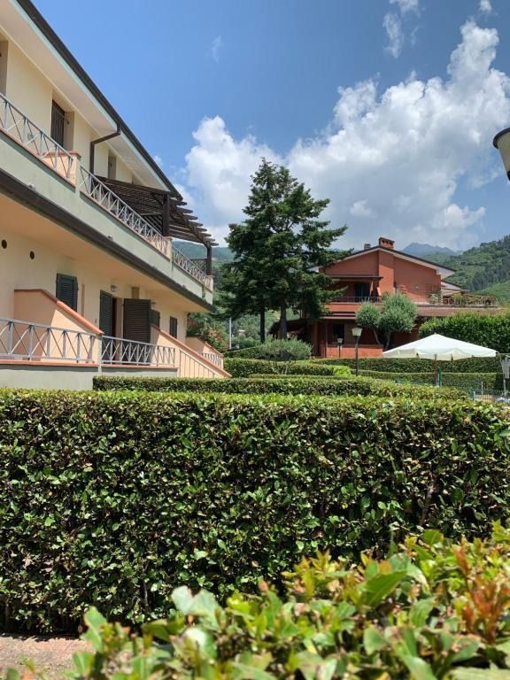 Edificio a due piani con balconi, siepi verdi, alberi e cielo azzurro con nuvole.