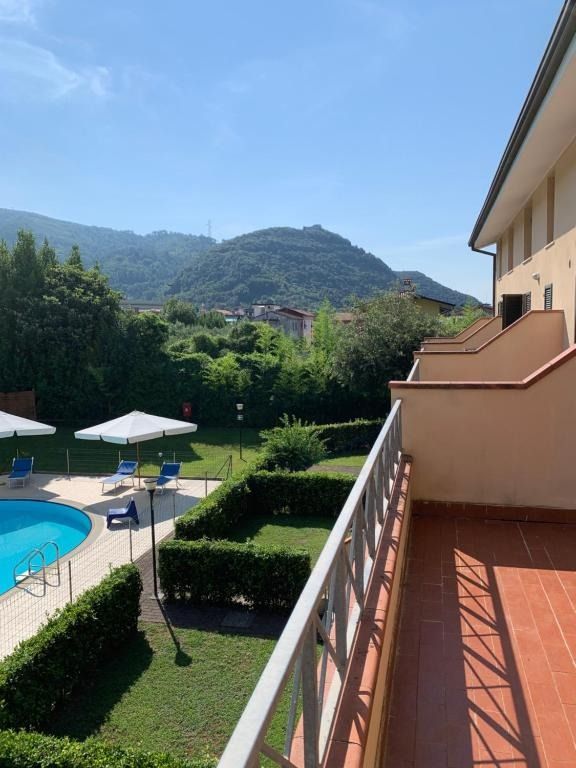 Vista dal balcone su piscina, siepi curate, montagne e cielo azzurro in una giornata di sole.