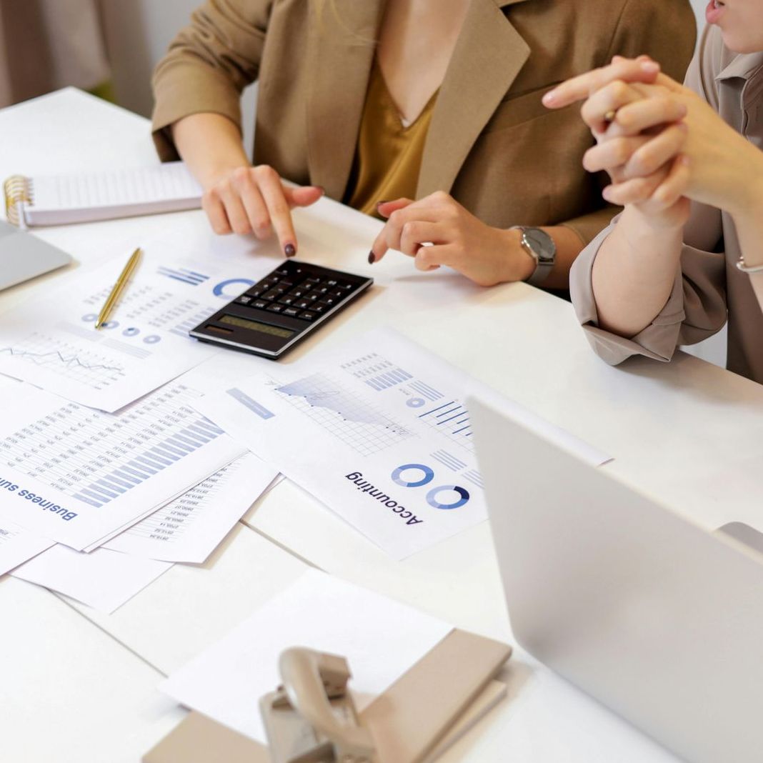 一位理財顧問正在為客人檢視保單及查看財務數據。桌上有文件、計算機和筆記型電腦。