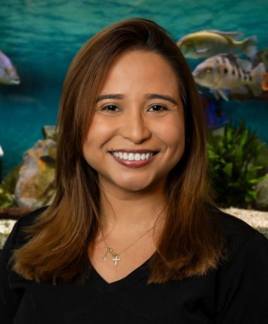 A woman is smiling in front of a fish tank.