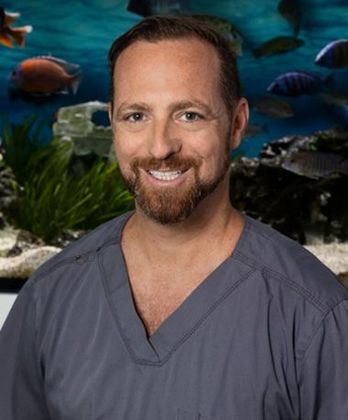 A man in a scrub is smiling in front of a fish tank.