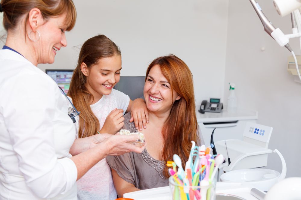 A dentist is talking to a woman and a girl in a dental office.