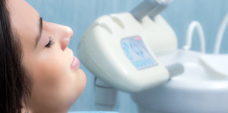 A woman is sitting in a dental chair looking at a machine.