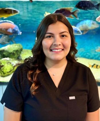 A woman in a black scrub top is smiling in front of a fish tank.