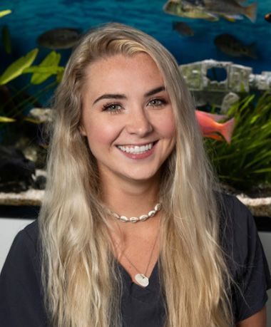 A woman is smiling in front of an aquarium with fish.