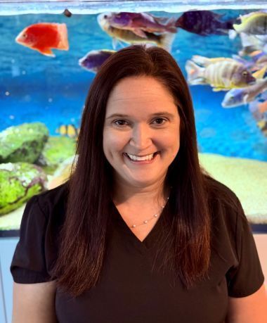 A woman is smiling in front of a fish tank.