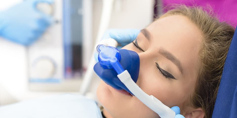 A woman is laying in a dental chair with an oxygen mask on her face.