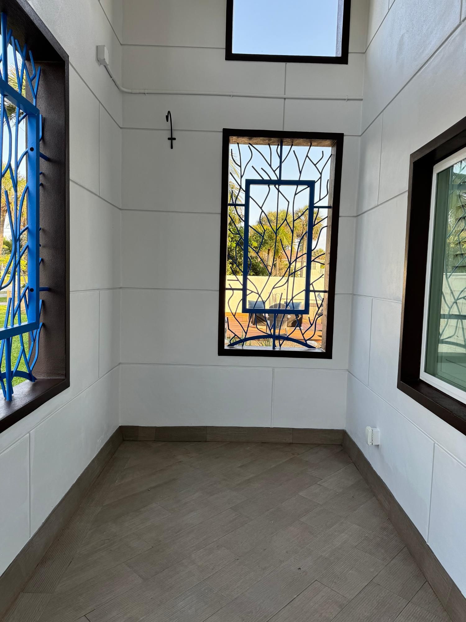 An indoor hallway featuring white block walls, tiled floors, and windows with decorative blue metal security bars.