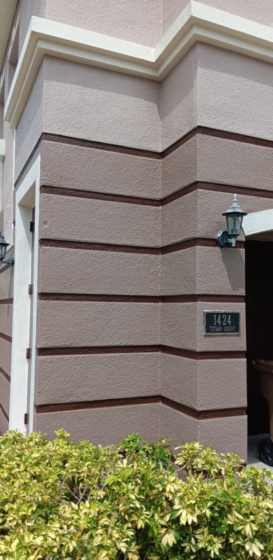 Beige building exterior with horizontal trim and a small address plaque reading 1120, next to a doorway and landscaping.