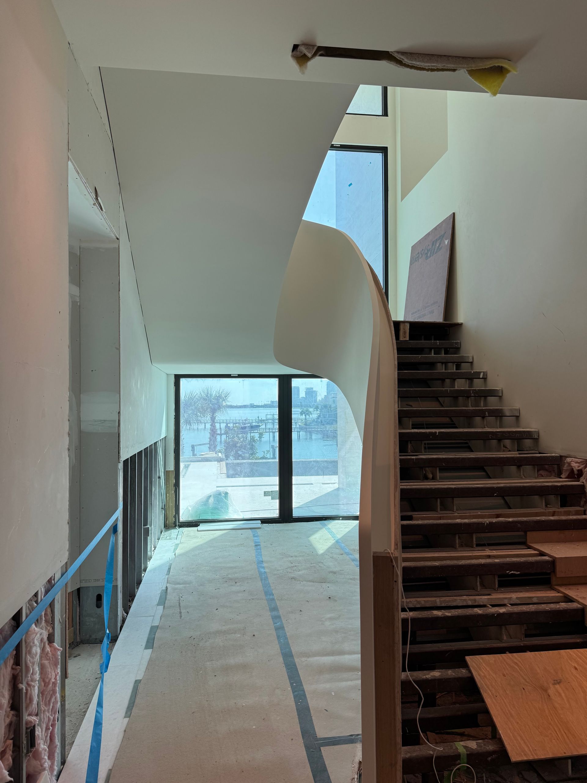 A curving staircase under construction in a bright, modern building overlooking a water view.