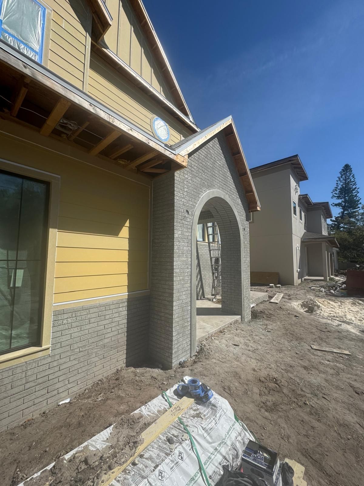 A new house under construction featuring a stone archway entrance and tan siding against a clear blue sky.