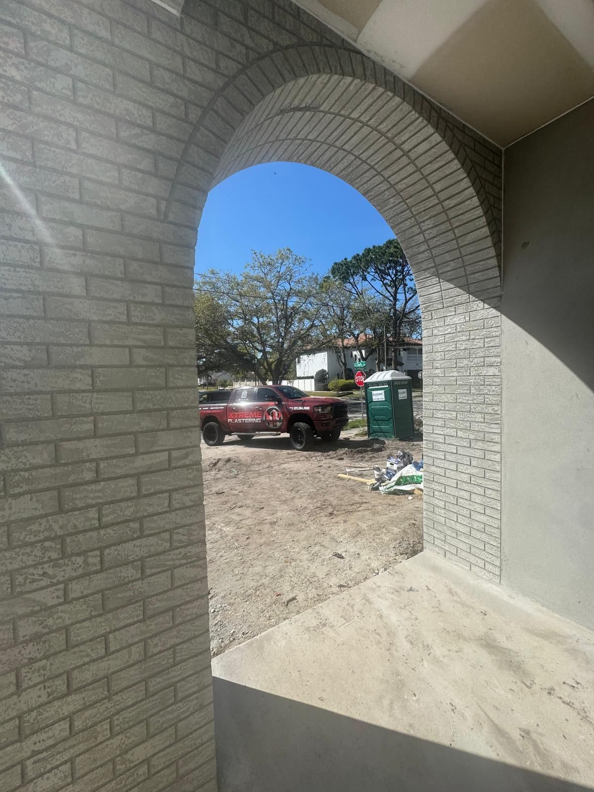 A view through a brick archway overlooking a construction site with a red truck and a portable toilet.