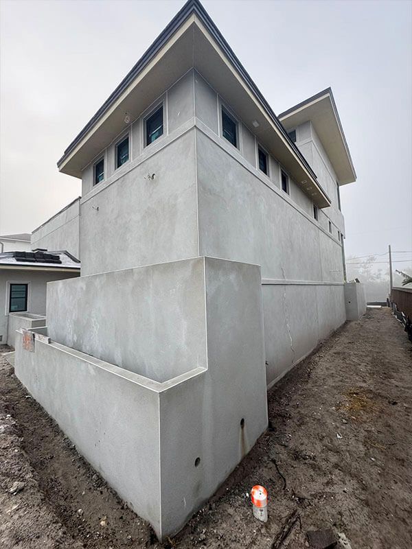 A modern, gray concrete multi-story building under construction with small high-set windows and dirt ground surroundings.