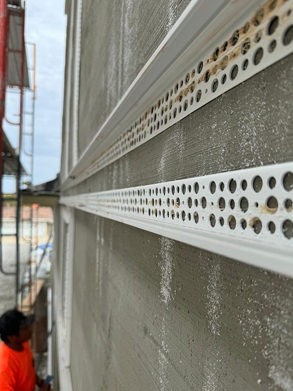 Close-up of white plastic trim beads installed on a grey stucco wall during building construction.