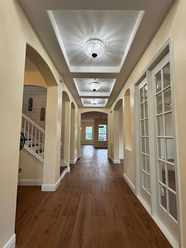 A hallway with wood floors, light-colored walls, arched entryways, and three recessed ceiling lights with glass fixtures.