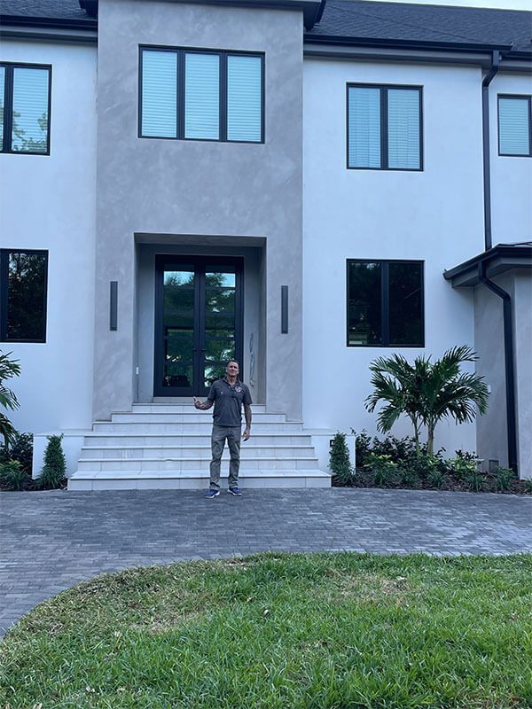 A bright indoor foyer with white paneled walls, white wicker furniture, tiled floors, and a blue decorative metal door.