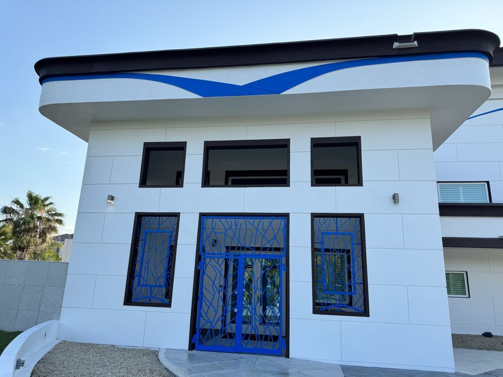 A white, modern building exterior with a blue, geometric-patterned metal door and matching accents under a blue sky.