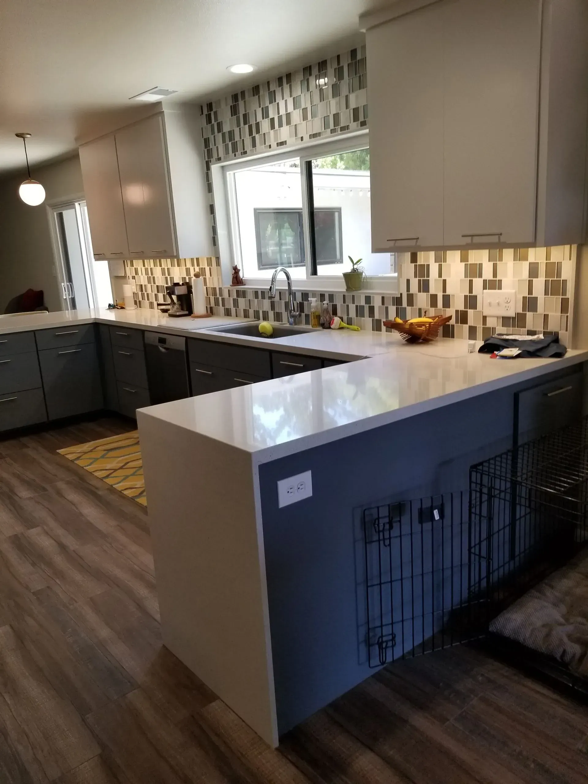 Modern kitchen with gray cabinets, white island countertop, tiled backsplash, and wood flooring.
