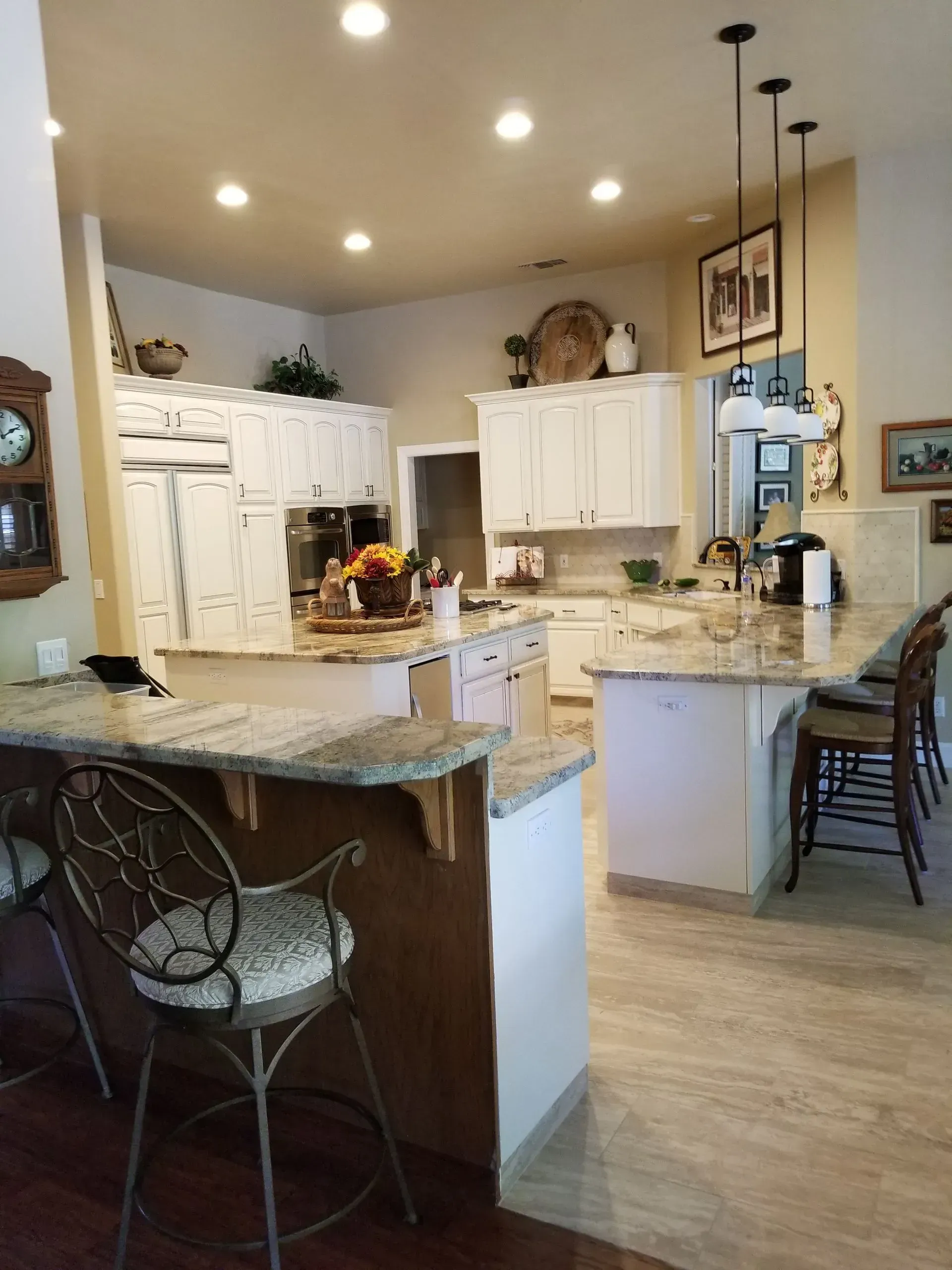 Bright kitchen with granite island, white cabinets, pendant lights, and wooden stools