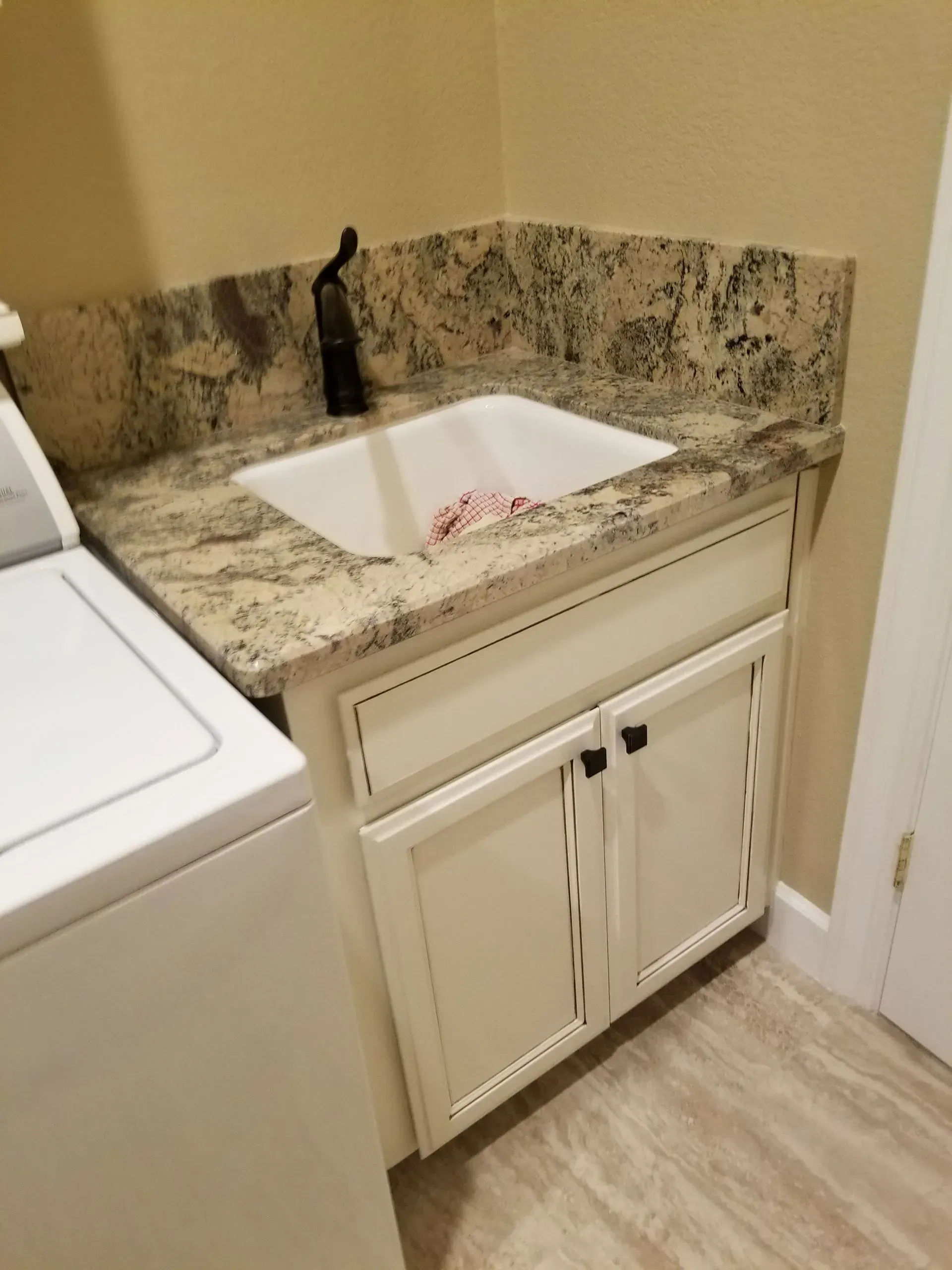 Bathroom vanity with granite countertop, white sink, and cabinet beside a washing machine.