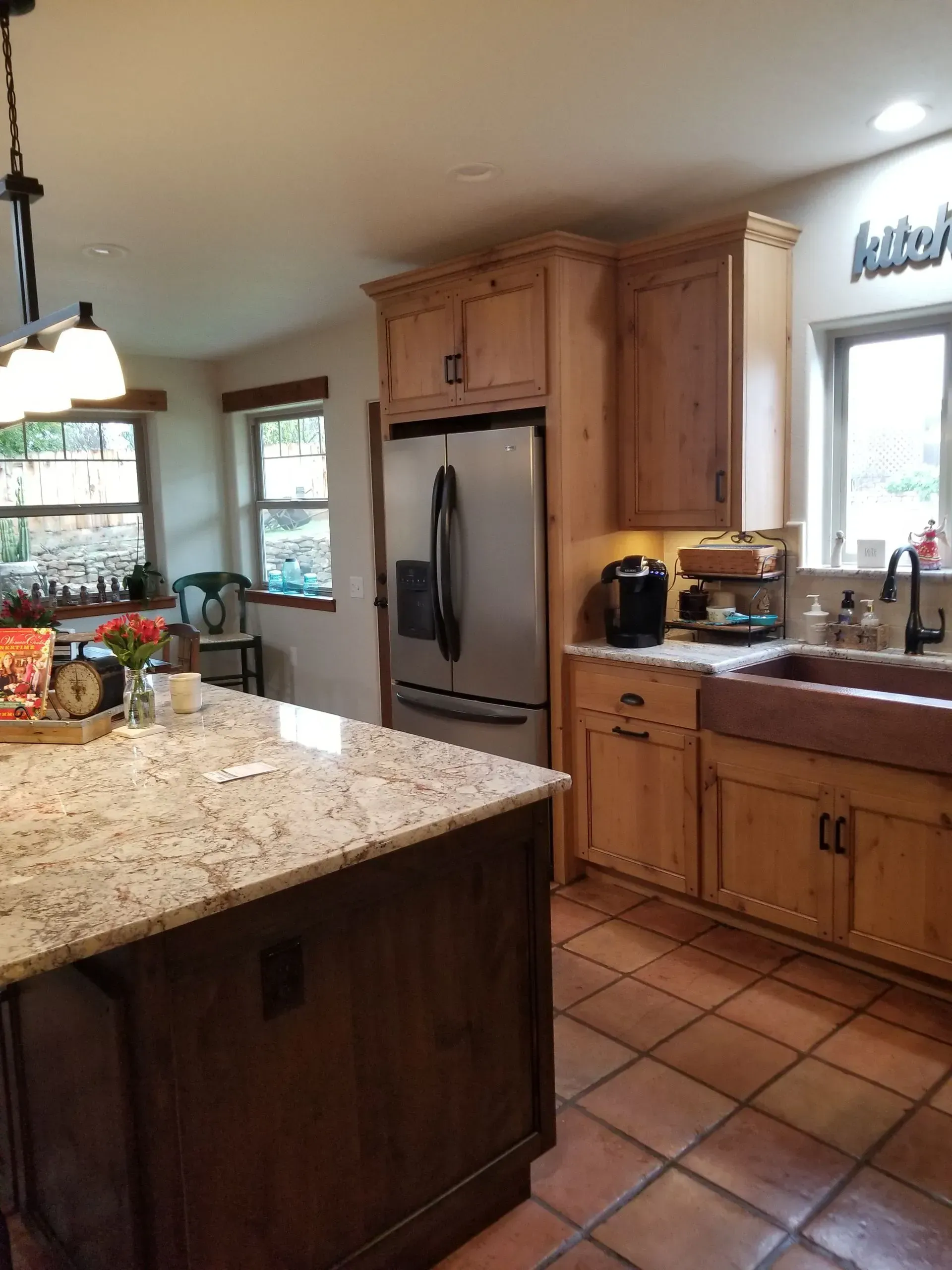 Bright kitchen with granite island, stainless fridge, wood cabinets, and tiled floor