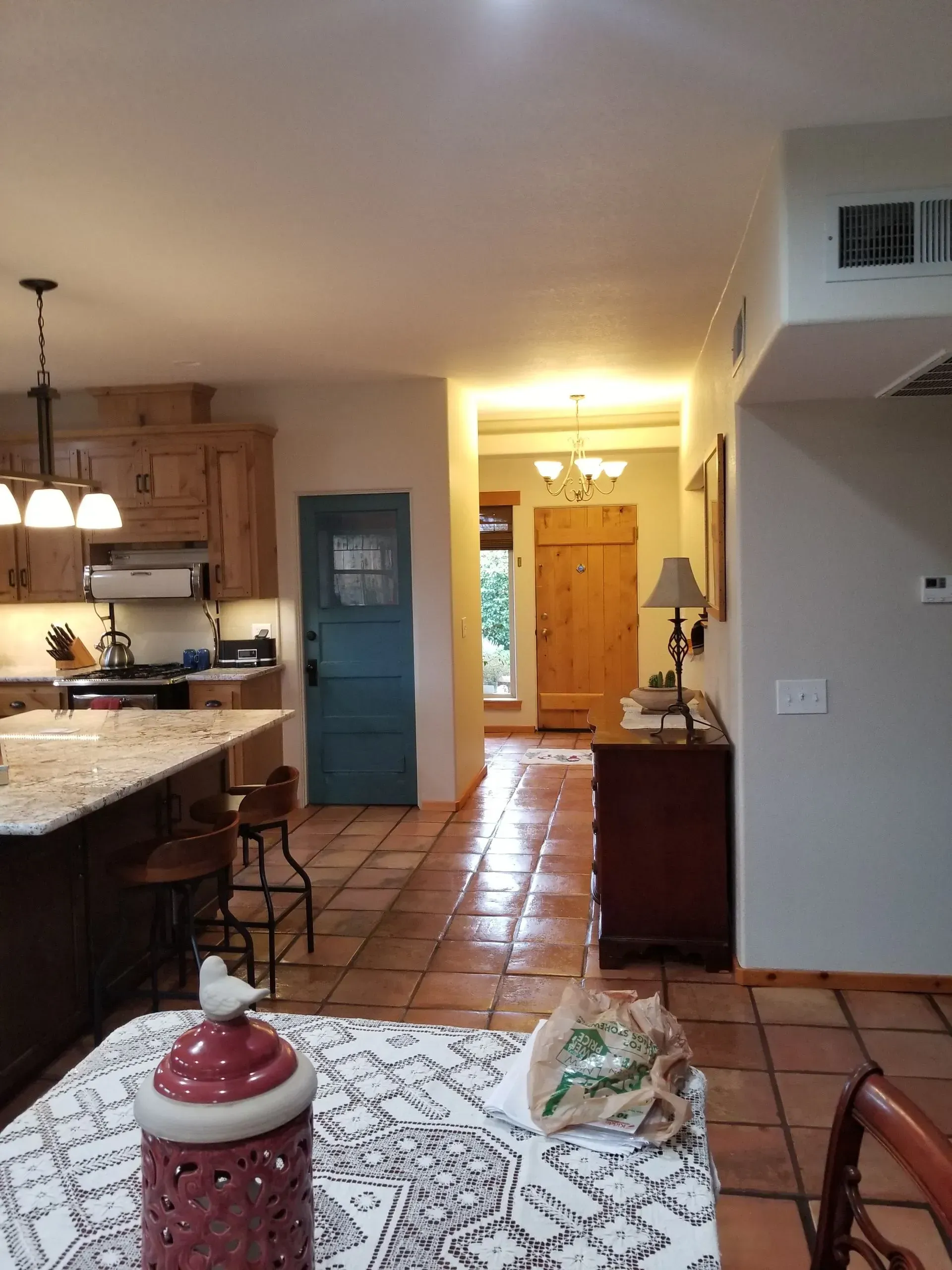 Cozy kitchen and hallway with terracotta tile floor, blue door, and lit entryway to the front door