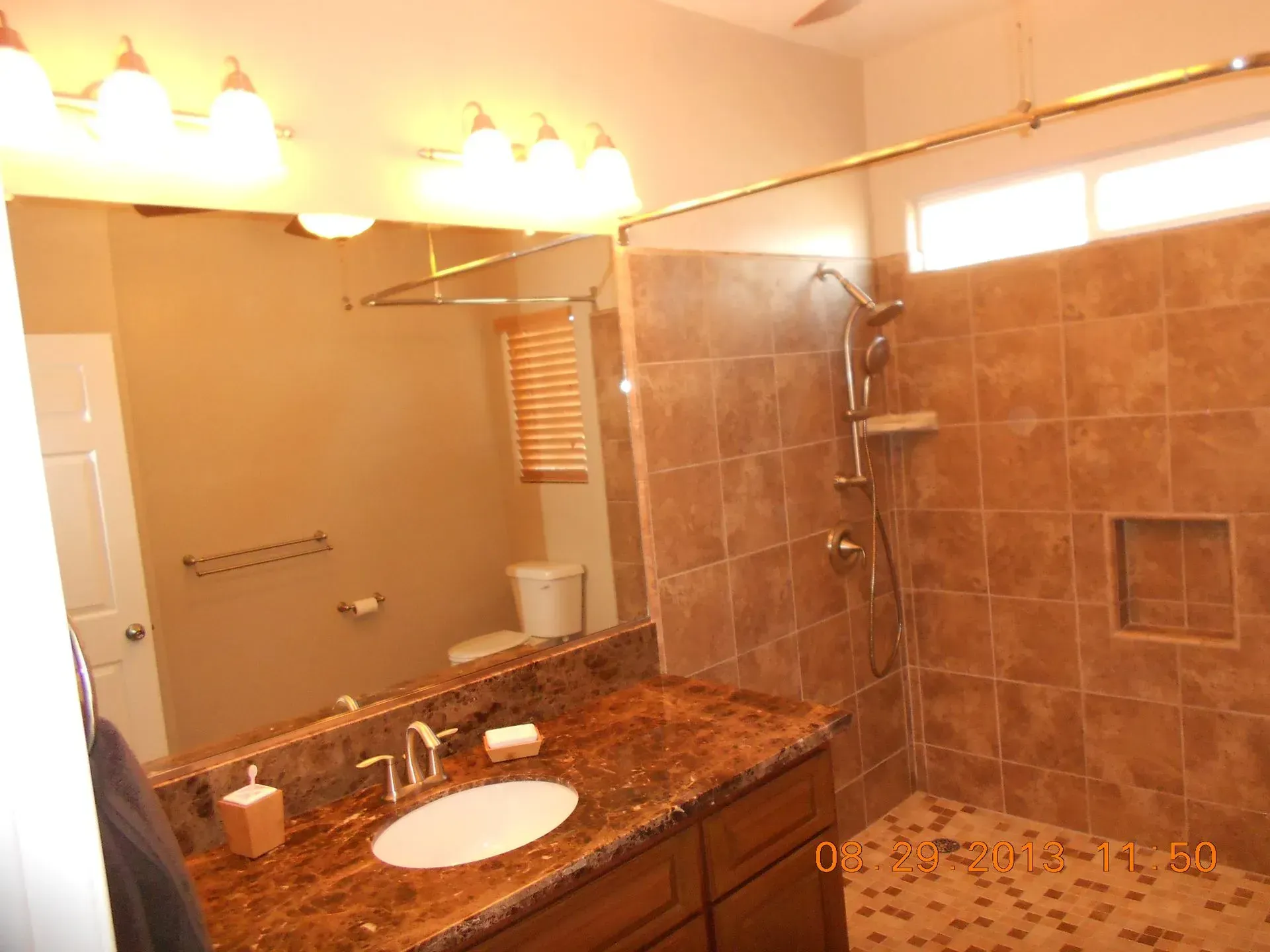 Bathroom with granite vanity, large mirror, wall lights, and tiled shower.