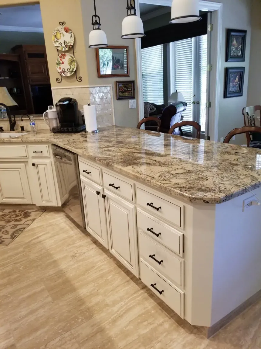 Bright kitchen with granite island, white cabinets, pendant lights, and large window blinds.