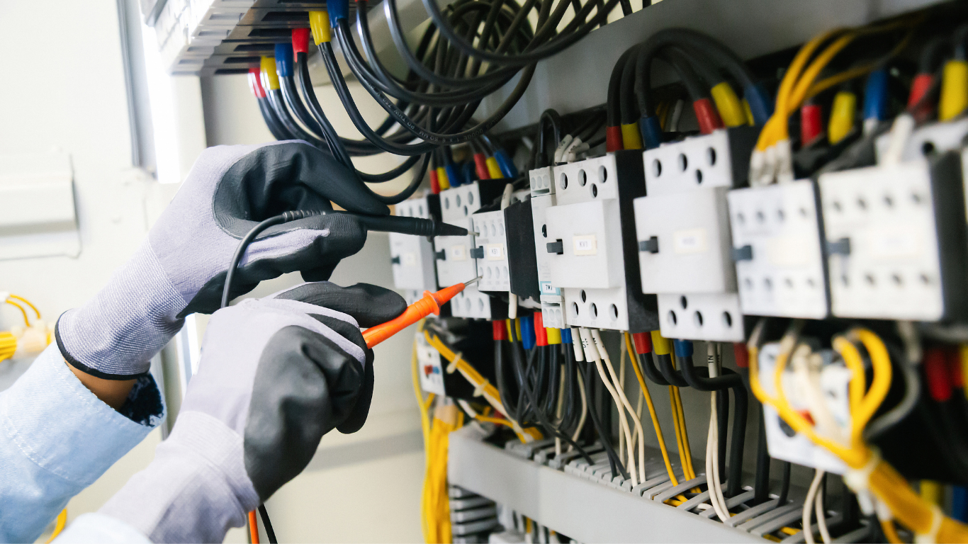 Electrician testing wiring in an electrical control panel with colored cables and circuit breakers