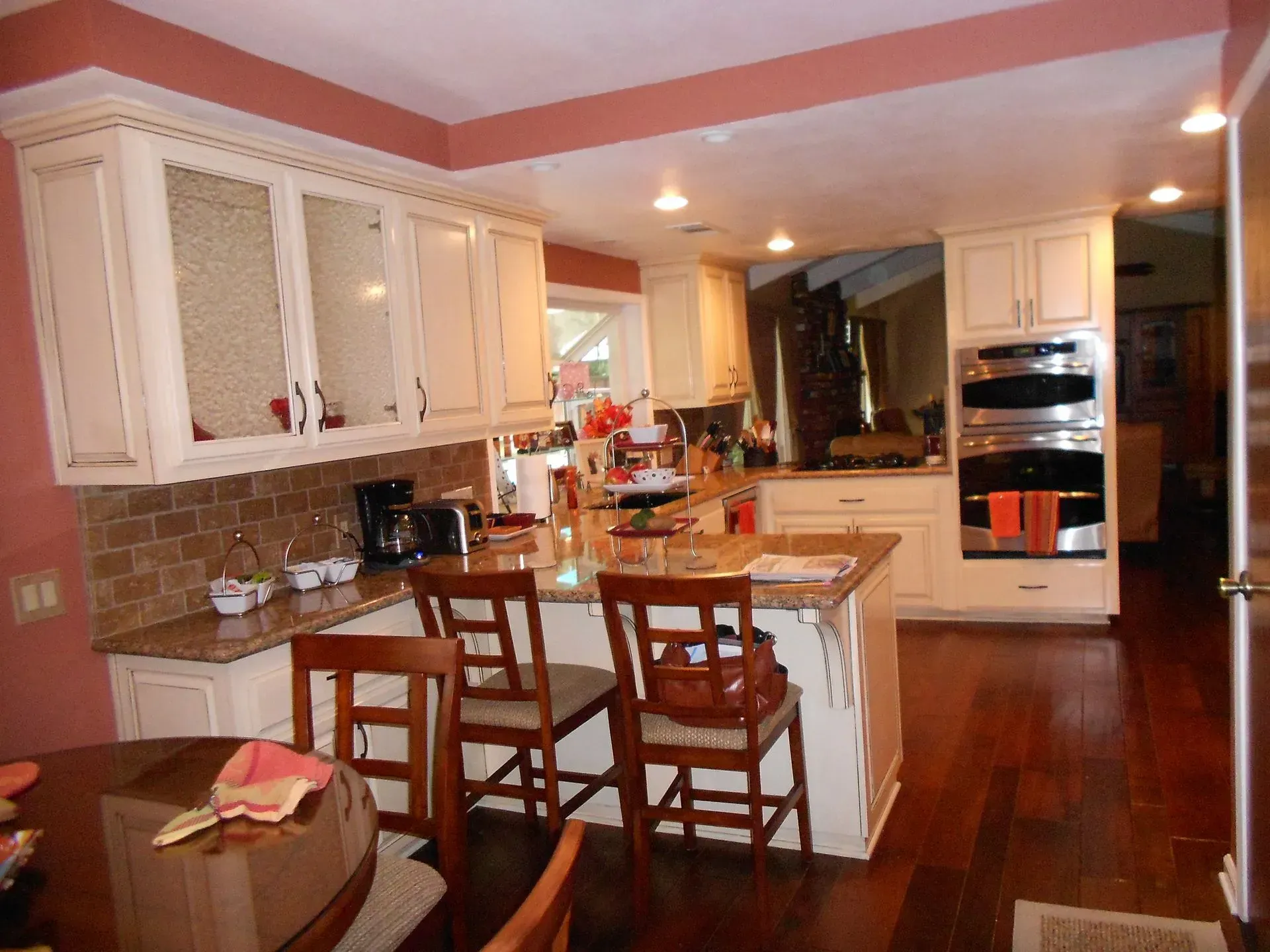 Warm kitchen with white cabinets, center island, wooden stools, and stainless steel oven in a home interior.