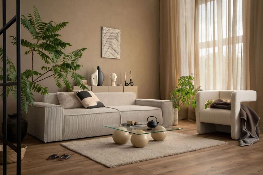 Neutral-toned living room with sofa, armchair, plants, and soft curtains in natural light