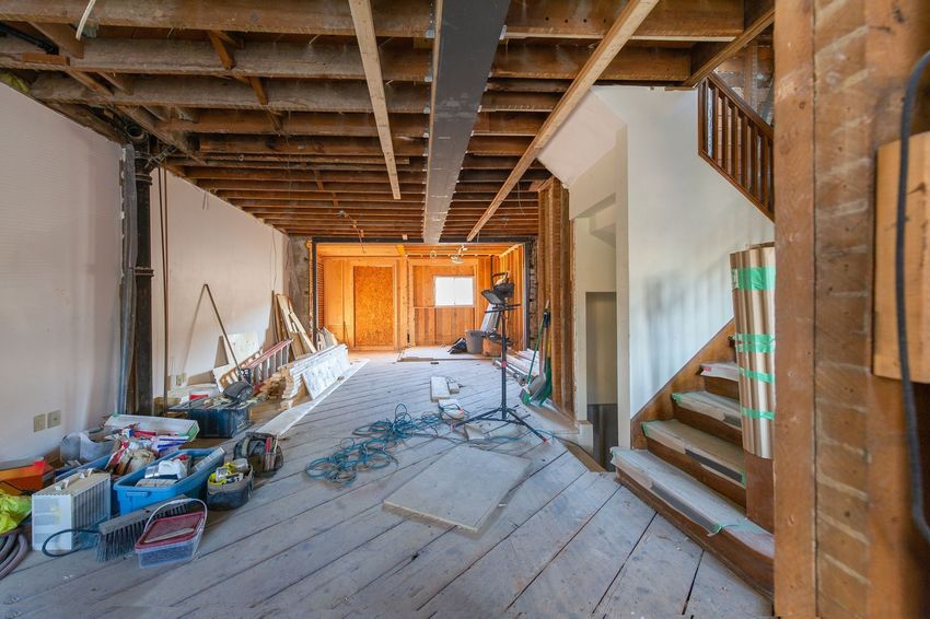 Renovation site with exposed beams, construction materials, and wooden stairs in a partially finished room