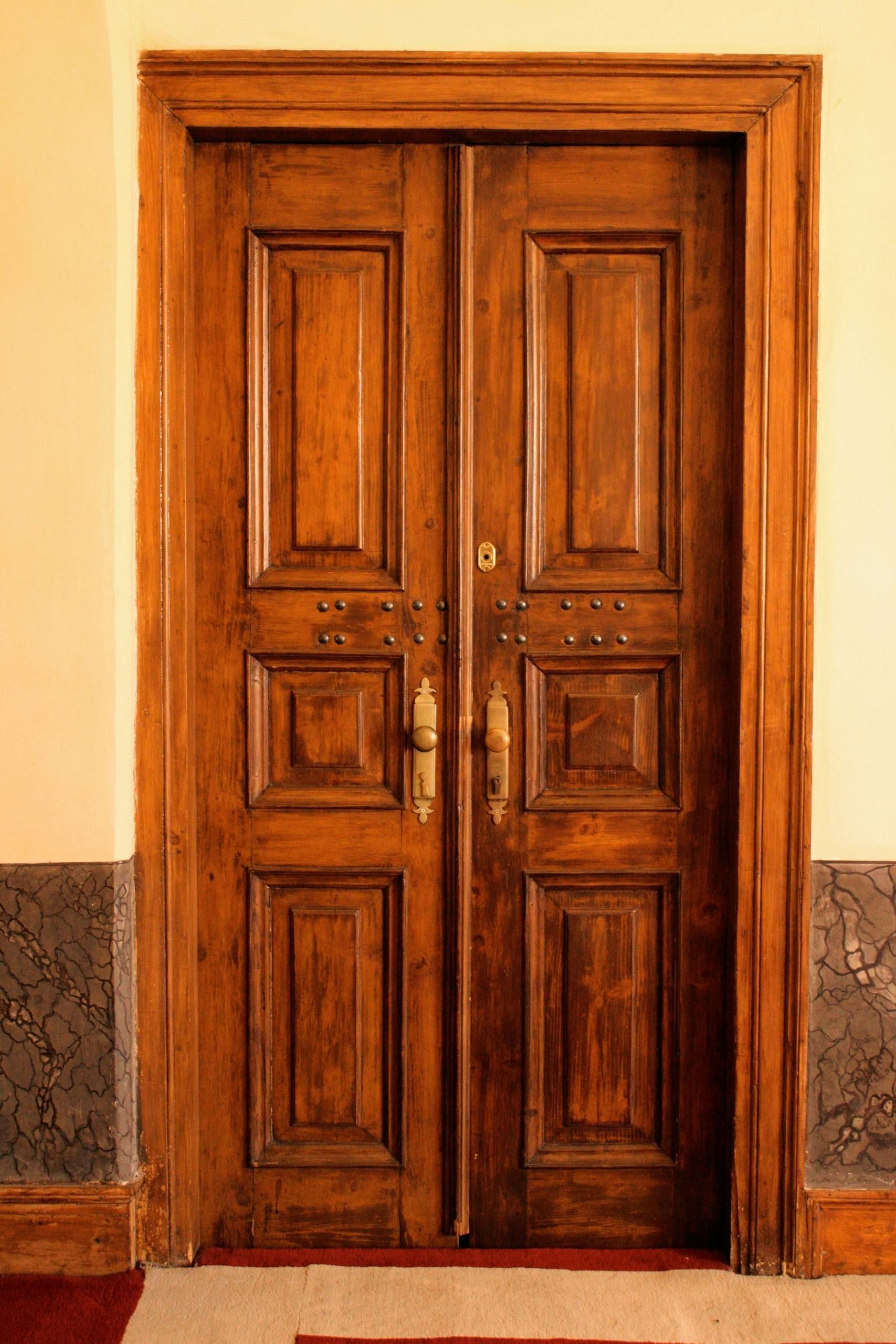 Wooden double doors with ornate panels in a stone doorway.