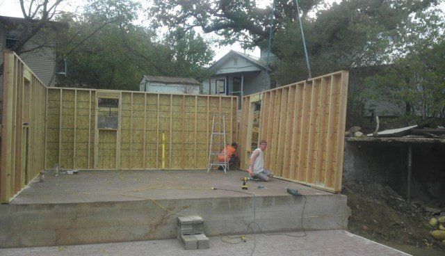 A man is kneeling on the ground in front of a building under construction.