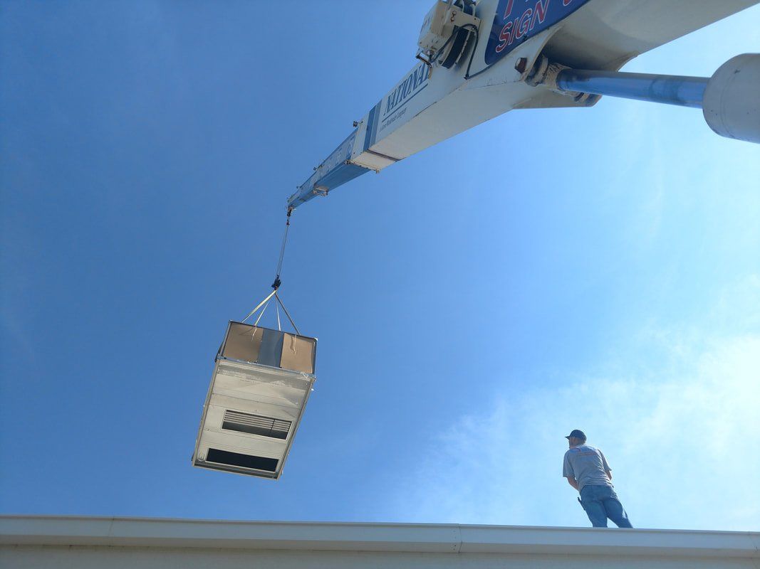 A man standing on a roof watching a crane lift a box