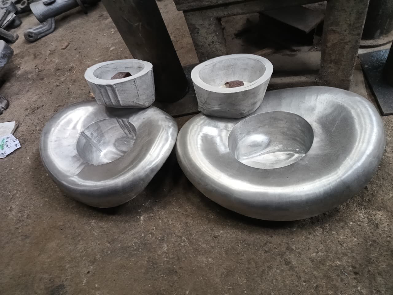 Dos piezas de metal fundido pulido, con forma de riñón y con cubetas centrales, reposan sobre el polvoriento suelo de un taller.