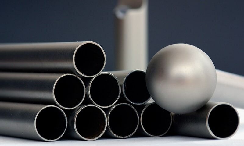 Un conjunto de tubos metálicos grises apilados junto a una esfera metálica lisa y redonda.