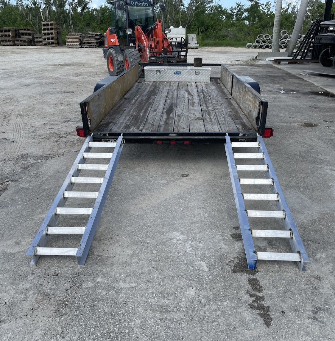 A trailer with ladder ramps attached to it and a tractor in the background