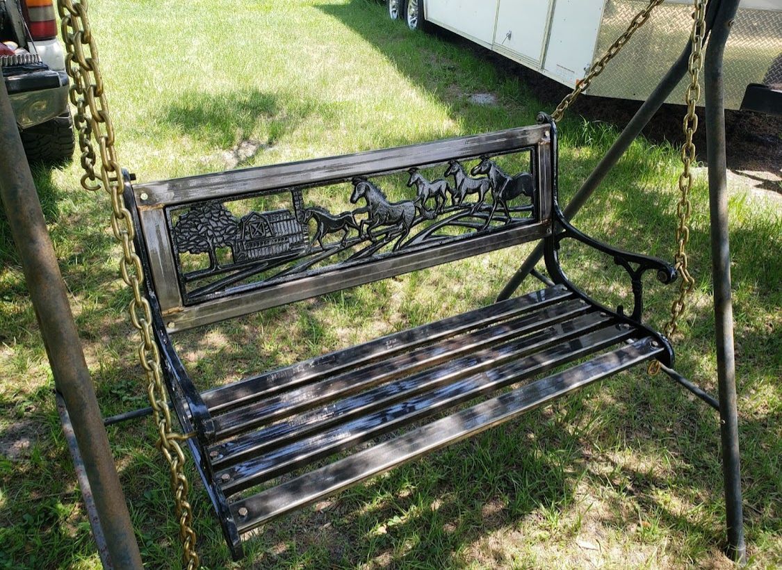 A black swing is sitting on top of a lush green field.