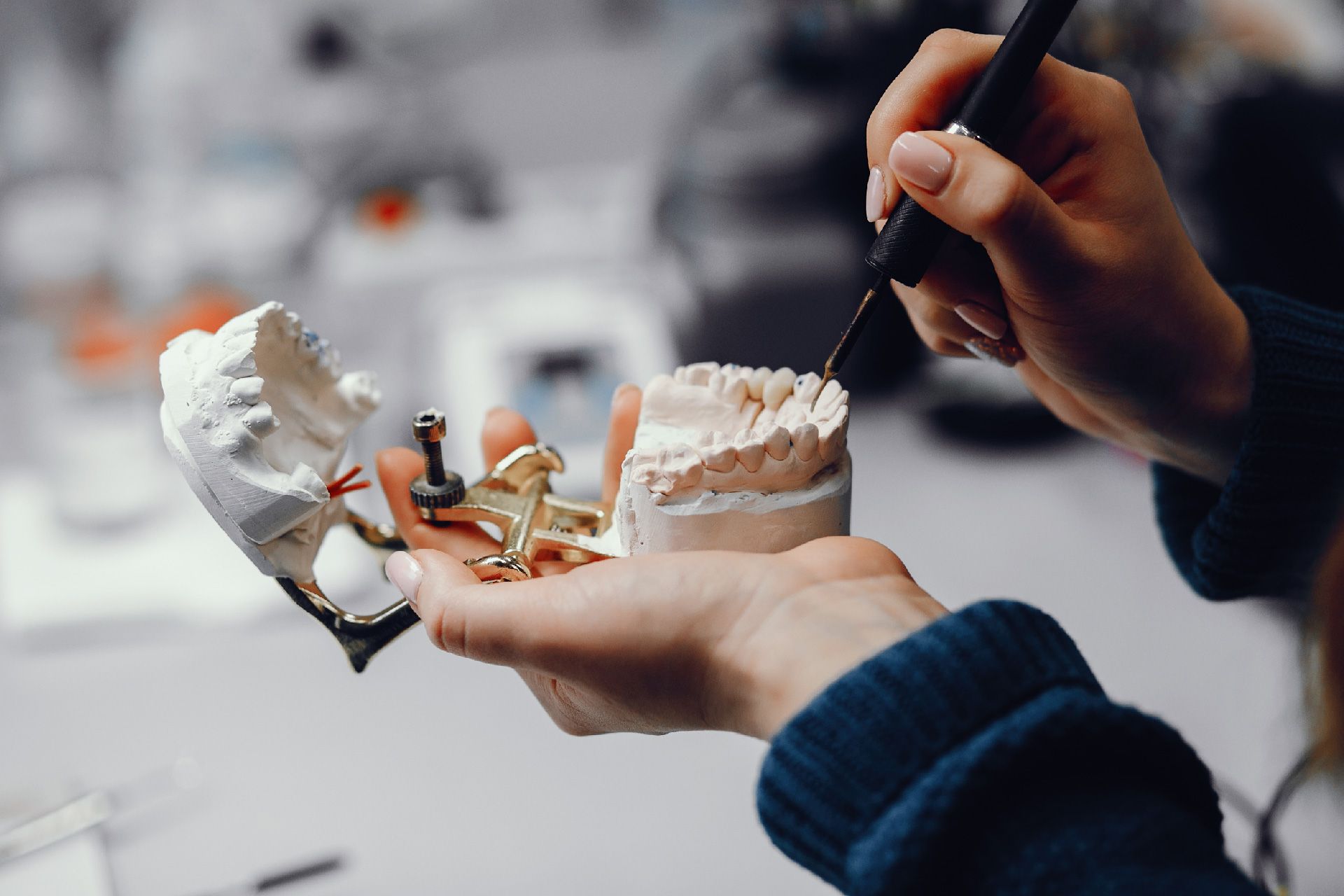 Persona trabajando en moldes dentales en un laboratorio, sosteniendo herramientas y modelos de yeso blanco.