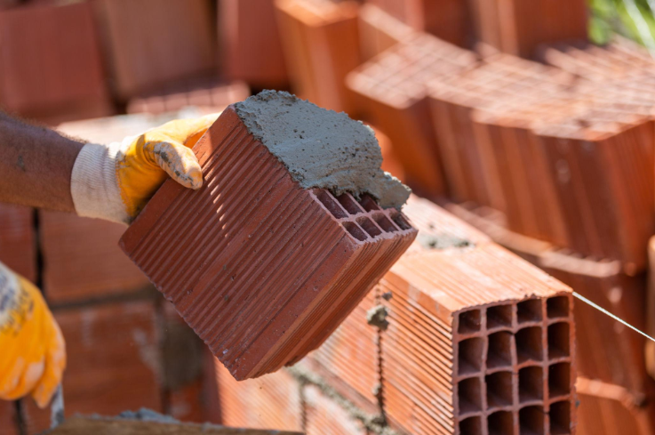 “Gloved hand spreading mortar on a red masonry block before placement during a masonry service in Friendswood, TX”