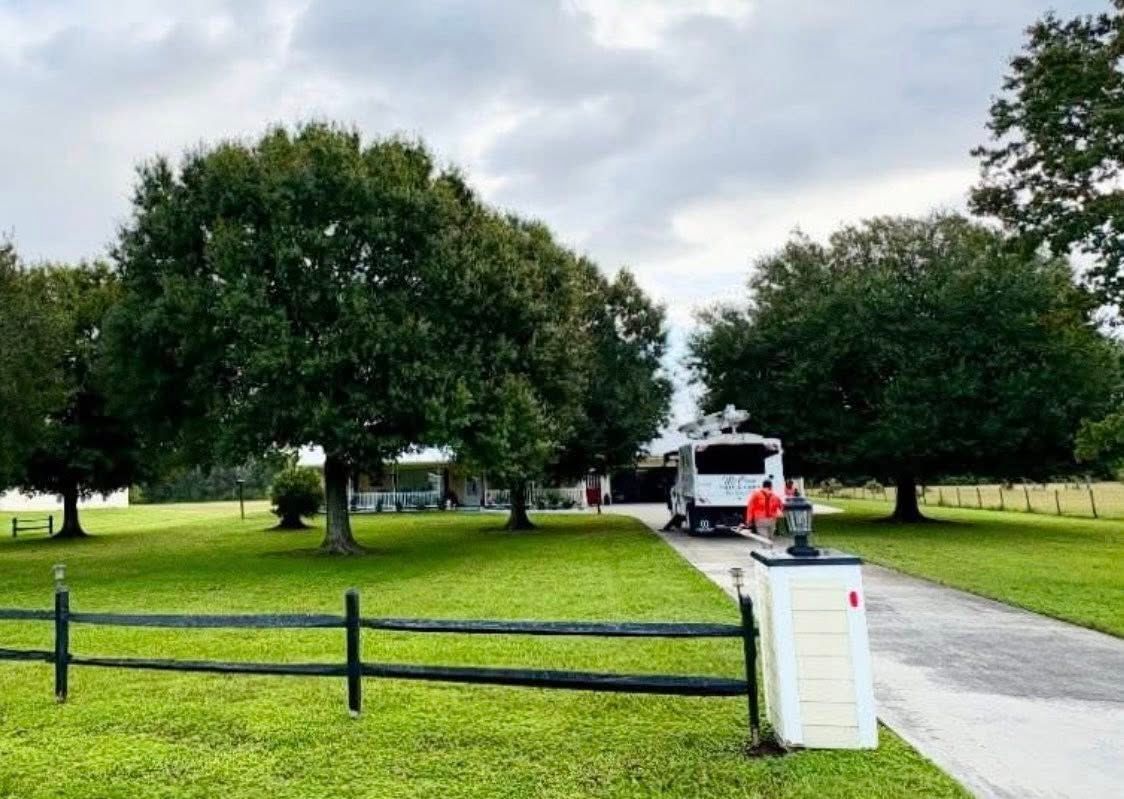 Green lawn with trees, house, and RV on a driveway. A fence and mailbox in the foreground.