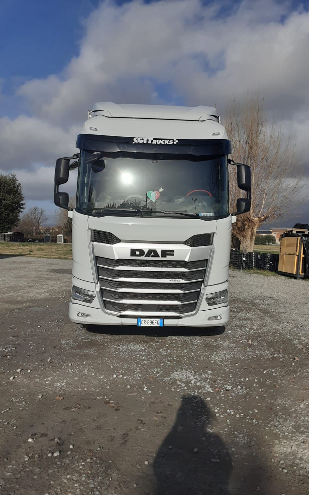 Un semirimorchio DAF bianco, visto frontalmente, parcheggiato su un piazzale ghiaioso sotto un cielo nuvoloso.