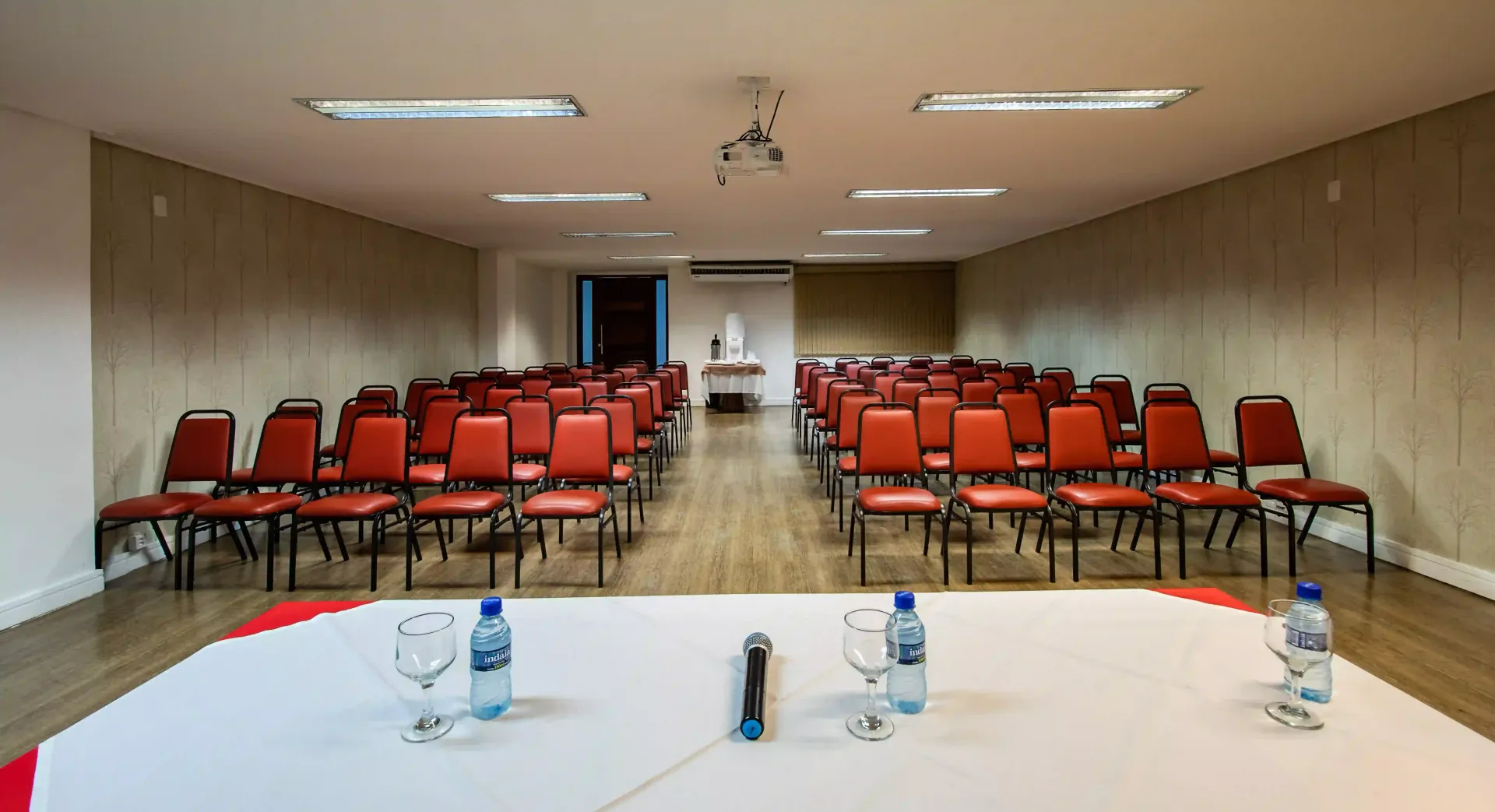 Uma sala de conferências com cadeiras vermelhas e uma mesa com garrafas de água. laguna-praia-hotel