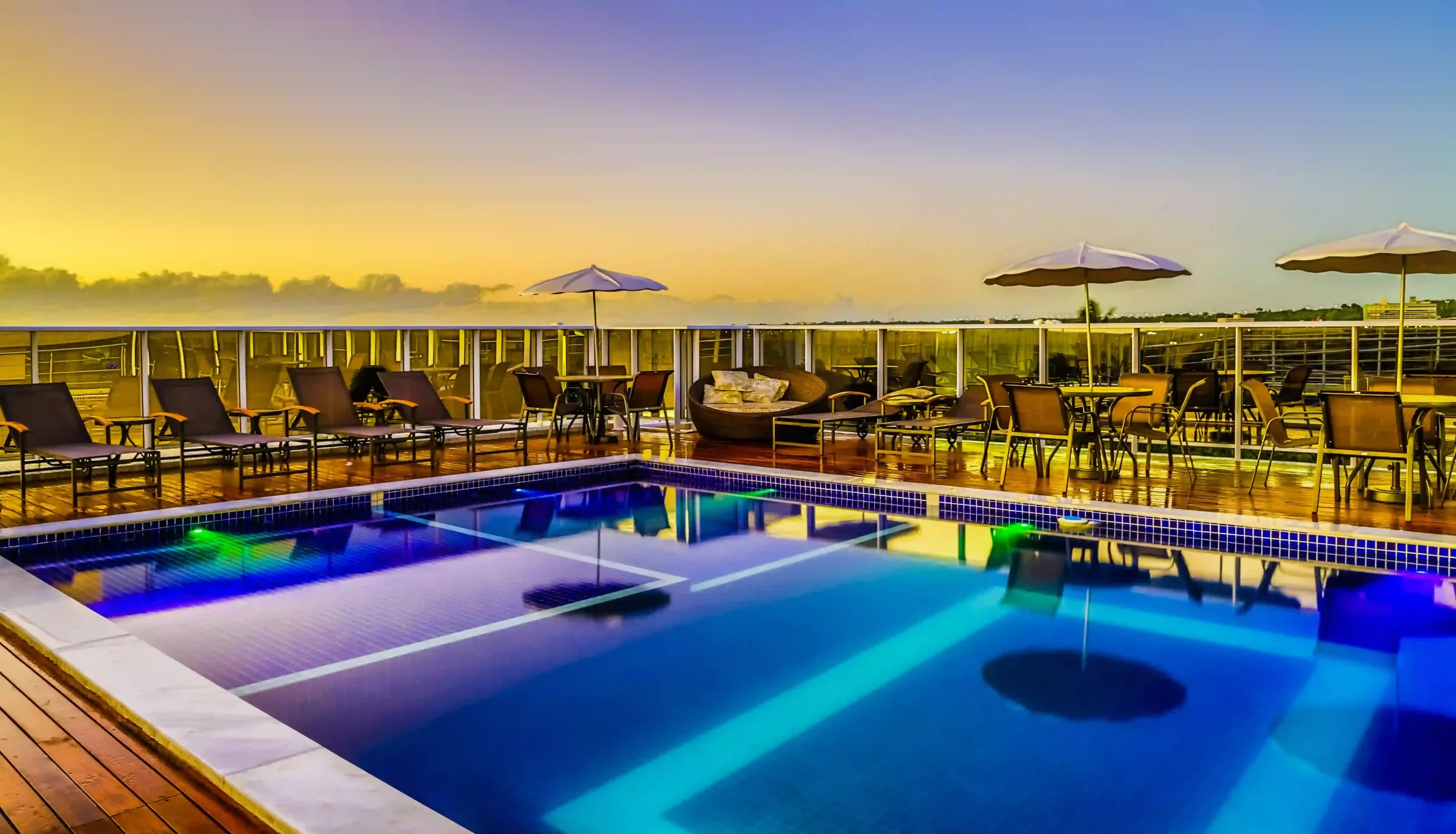 Uma grande piscina cercada por cadeiras e guarda-sóis ao pôr do sol.laguna-praia-hotel