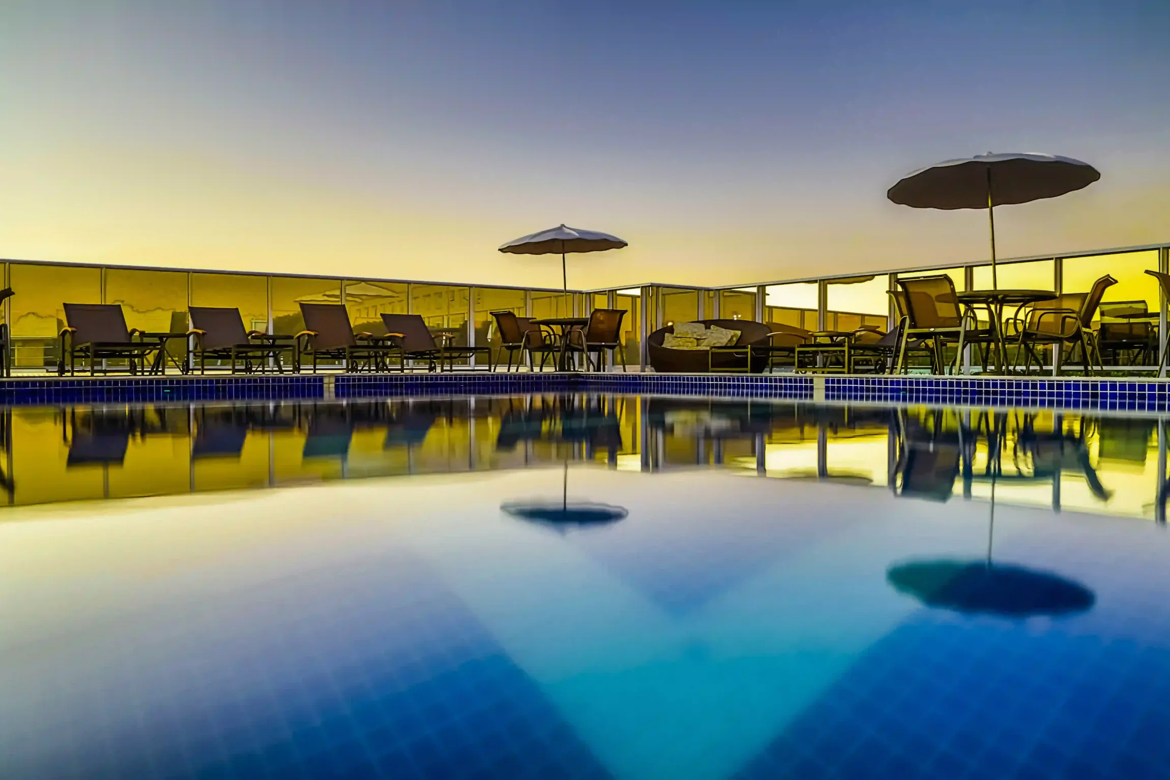 Uma piscina com guarda-sóis e cadeiras ao redor ao pôr do sol.