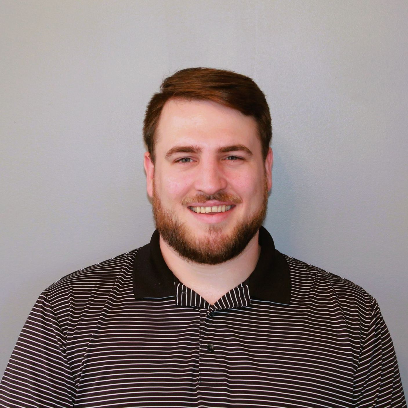 A man with a beard is wearing a black and white striped shirt and smiling.