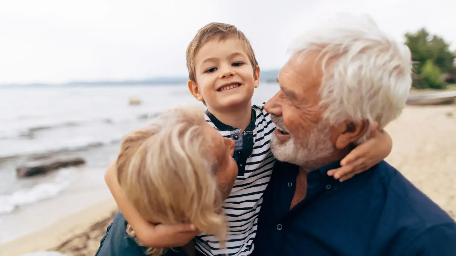 An elderly man is holding two children on the beach.