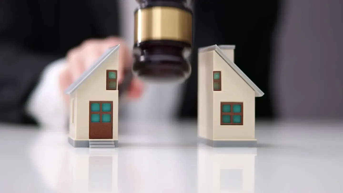 A person is holding a judge 's gavel over two small houses.